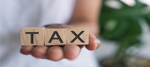 Close-up of hand holding blocks that spell 'TAX,' representing the importance of understanding taxes.