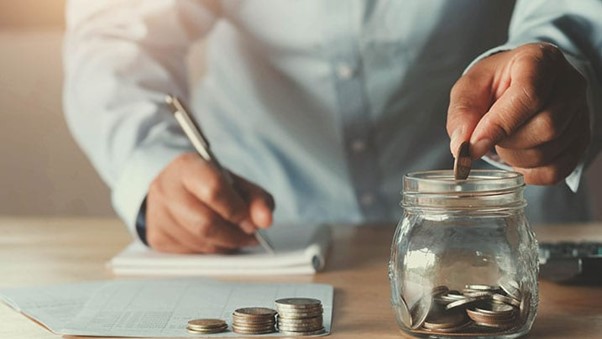 Person placing coins into a glass jar, symbolizing saving a portion of income for future needs