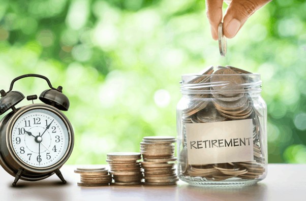 Coins in a jar labeled 'Retirement' next to a clock, symbolizing the importance of starting to save for retirement early.